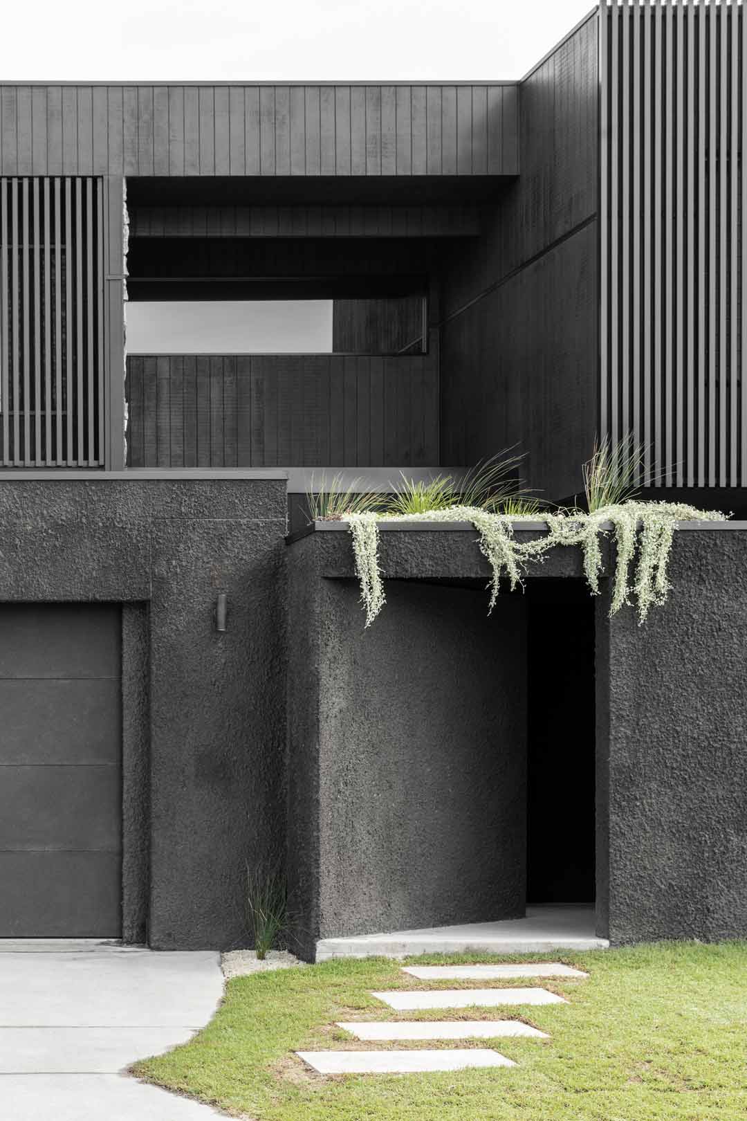 A-black-rendered-house-exterior-with-hanging-green-plants-and-steel-privacy-battons