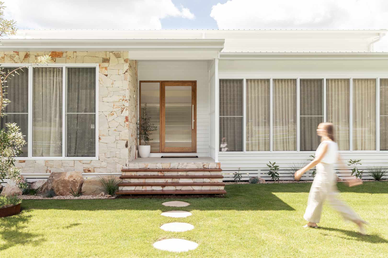 A-modern-house-entry-way-with-limestone-crazy-pave-stone-feature-wall-simple-garden-and-a-timber-door-with-fluted-glass