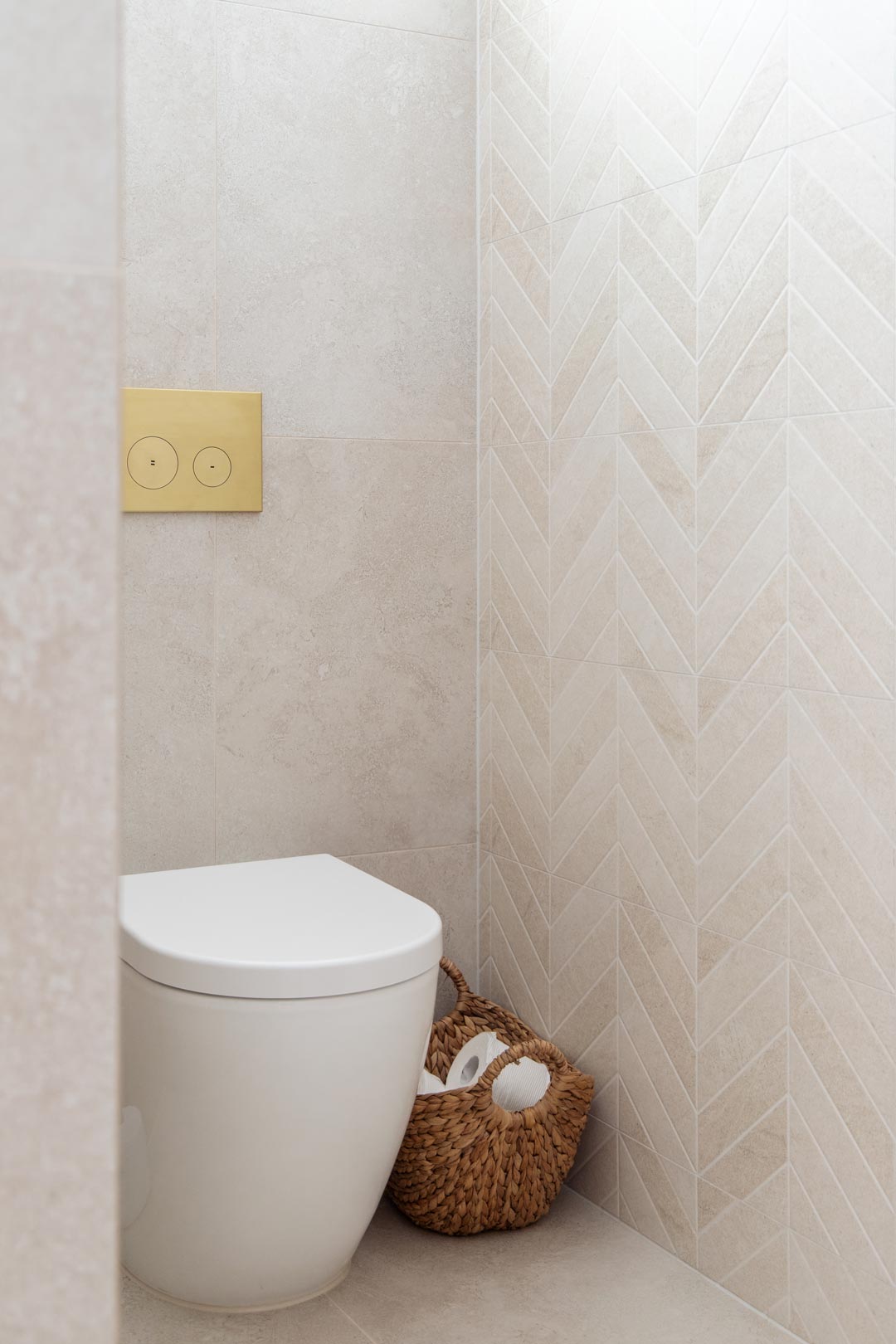 A-warm-powder-room-toilet-space-with-brushed-brass-flush-button-and-soft-herringbone-tiles-and-woven-basket-to-keep-toilet-rolls-organised