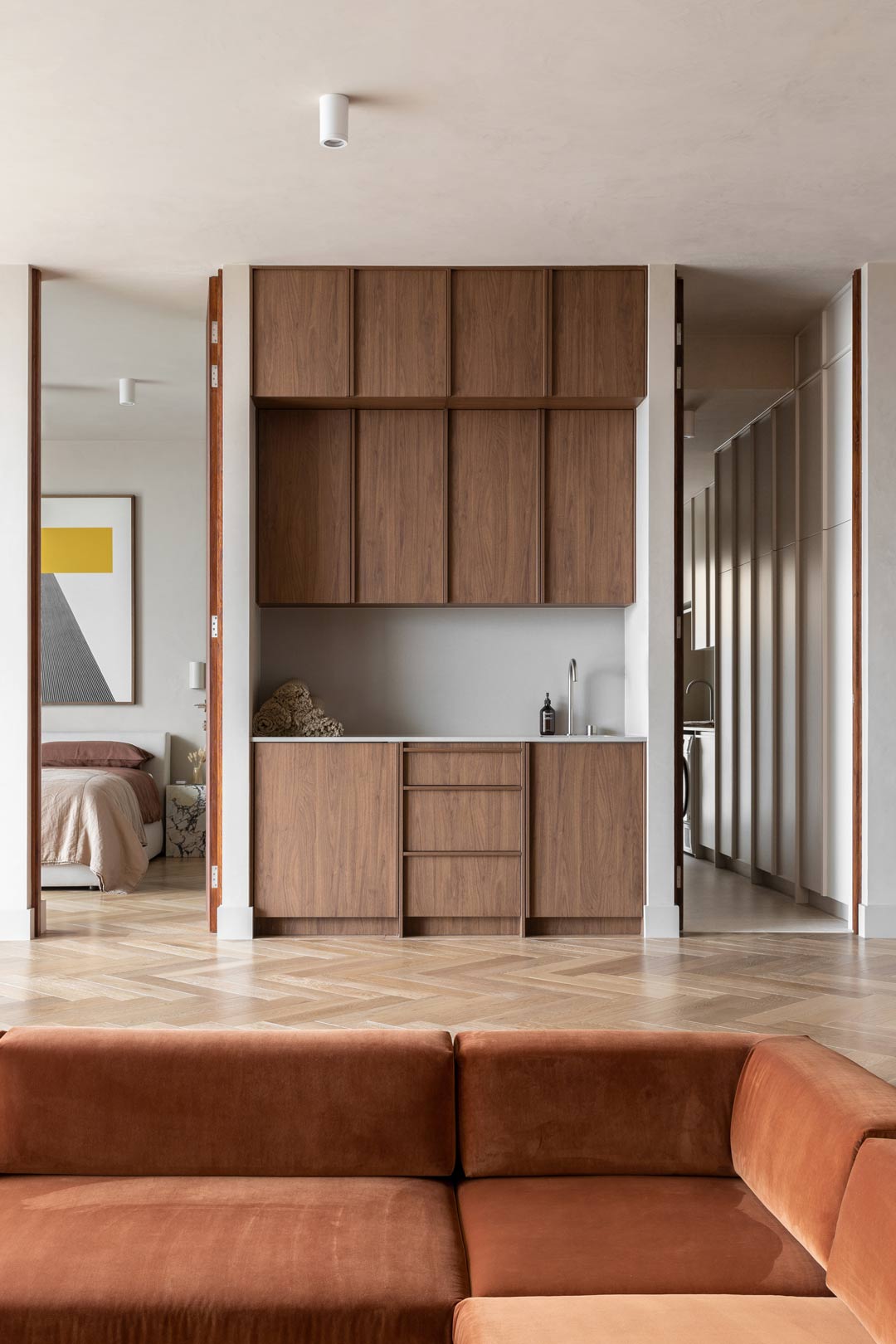 An-open-plan-living-room-and-bar-area-with-a-rust-velvet-sunken-lounge-positioned-with-a-rich-earthy-neutral-bedroom-and-laundry-with-walnut-cabinetry-and-timber-parquet-flooring.jpg